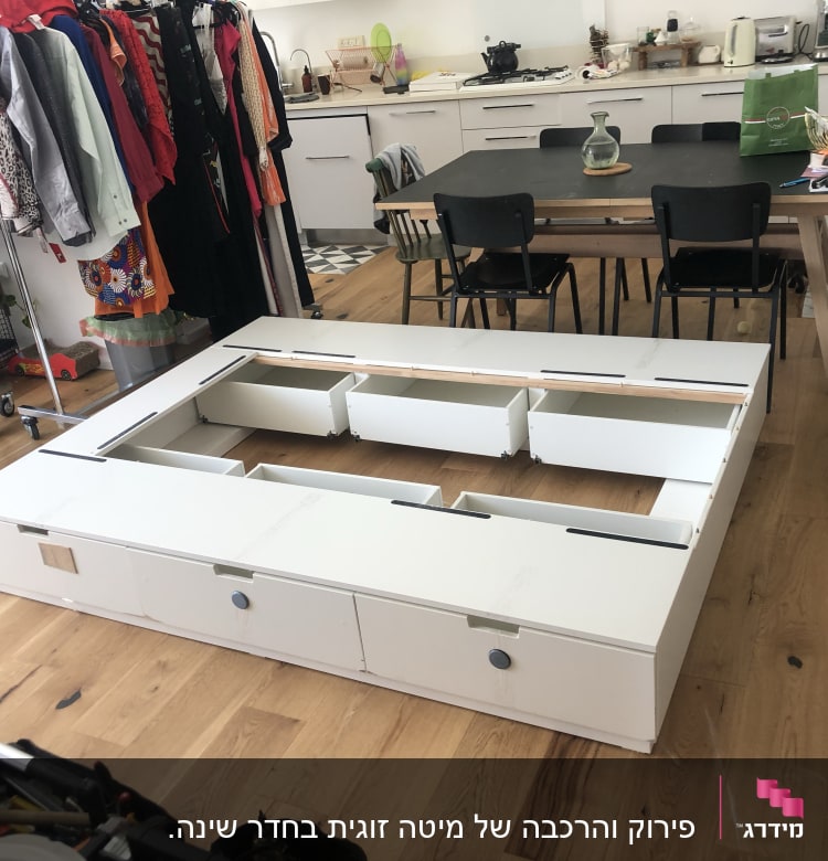 מסגרת מיטה לבנה עם מגירות פתוחות על רצפת עץ